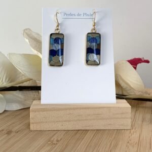 Boucles d'oreilles pendantes rectangulaires en marqueterie de paille bleue et beige de face sur support blanc
