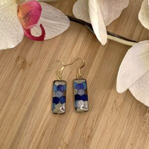Paires de boucles d’oreilles en marqueterie de paille bleue et beige posées à plat sur bois avec fleur Paires de boucles d’oreilles en marqueterie de paille bleue et beige posées à plat sur bois avec fleur